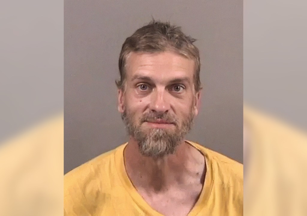 A person with short hair and a beard wearing a yellow shirt is shown in a mugshot-style photograph against a plain background.